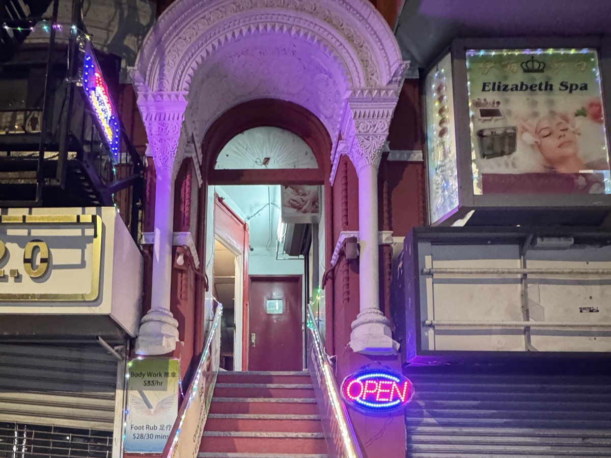 The street entrance at 7 Elizabeth Street at night: a lit stone archway over a red staircase leading up to the door, with a red neon OPEN sign and an Elizabeth Spa lightbox beside it.