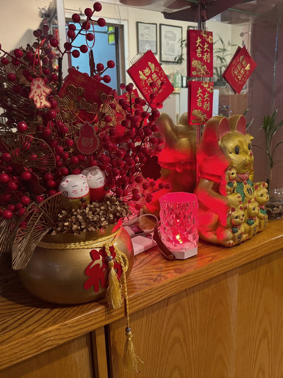 A reception shelf decorated for lunar new year: red berry branches in a gold pot, gold rabbit figurines and hanging red good-fortune envelopes.