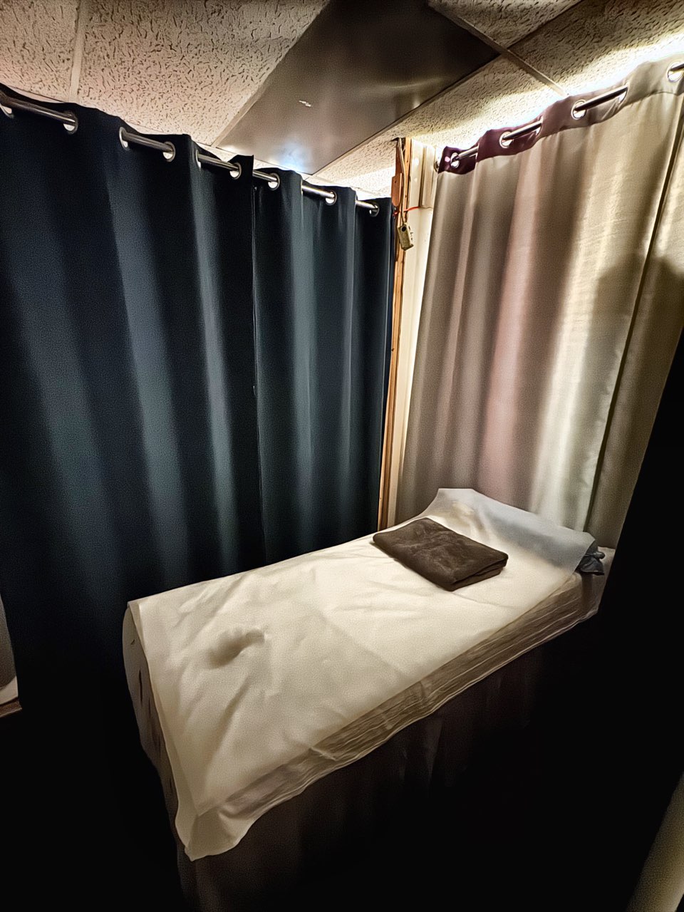 A single treatment cubicle at Elizabeth Spa, curtained on two sides, with a massage bed made up in white linen and a folded towel.
